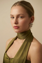 A model with a soft autumn complexion wearing silver botanical pearl earrings styled with an olive green silk scarf. The floral drop earrings frame the face elegantly
