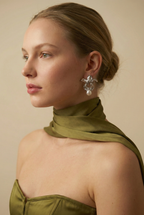 A model with a soft autumn complexion wearing silver botanical pearl earrings styled with an olive green silk scarf. The floral drop earrings frame the face elegantly