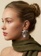 Close-up of sculptural silver orchid earrings featuring a high-luster real white pearl drop. The textured metal petals mimic a blooming iris flower, perfect for bridal jewelry or statement wear