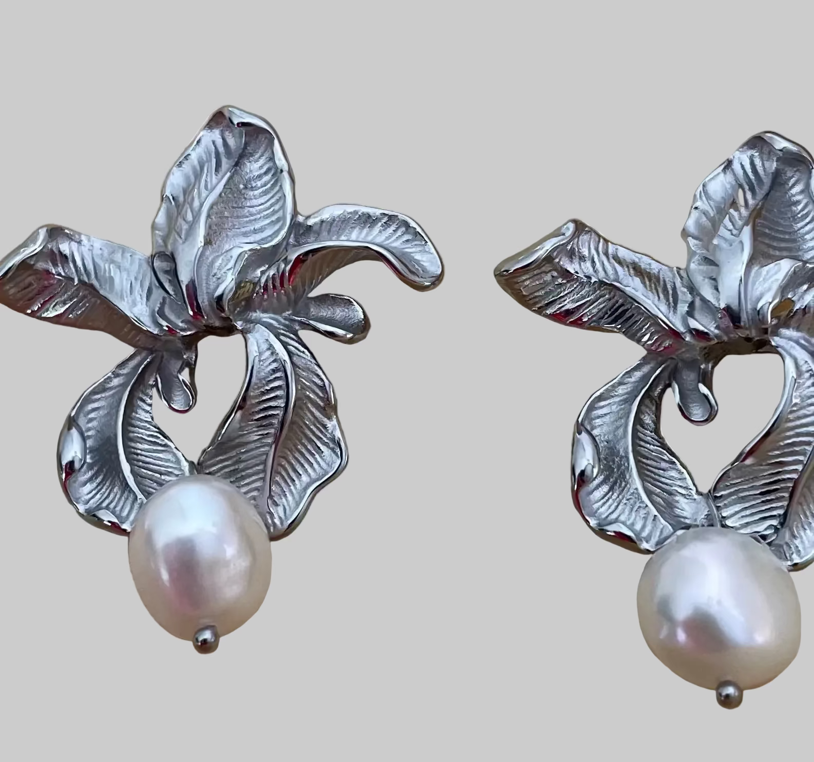 Macro detail showing the intricate textures of handcrafted silver flower earrings and the iridescence of the freshwater pearl attached