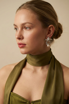 A model with a soft autumn complexion wearing silver botanical pearl earrings styled with an olive green silk scarf. The floral drop earrings frame the face elegantly