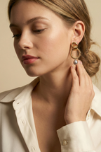 Close-up detail of textured gold interlocking hoop earrings featuring a lustrous metallic grey pearl drop. The design includes a beaded gold circle and polished gold links