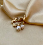 Close-up of textured gold huggie hoop earrings featuring a lustrous white pearl drop. The earrings have an organic, hammered gold finish