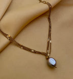 Close-up of a delicate triple-strand gold chain necklace featuring a single grey baroque pearl pendant