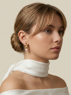 Elegant jewelry styling inspiration: Chunky gold twisted knot studs with pink pearl drops. Close-up side profile shot of a model wearing luxury pearl earrings with a white dress. Perfect for bridal or everyday elegance.