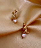 Pair of gold-knot earrings with pearls on a beige fabric background