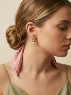 Elegant jewelry styling inspiration: Chunky gold twisted knot studs with pink pearl drops. Close-up side profile shot of a model wearing luxury pearl earrings with a green cami and polka dot scarf. Perfect for bridal or everyday elegance.