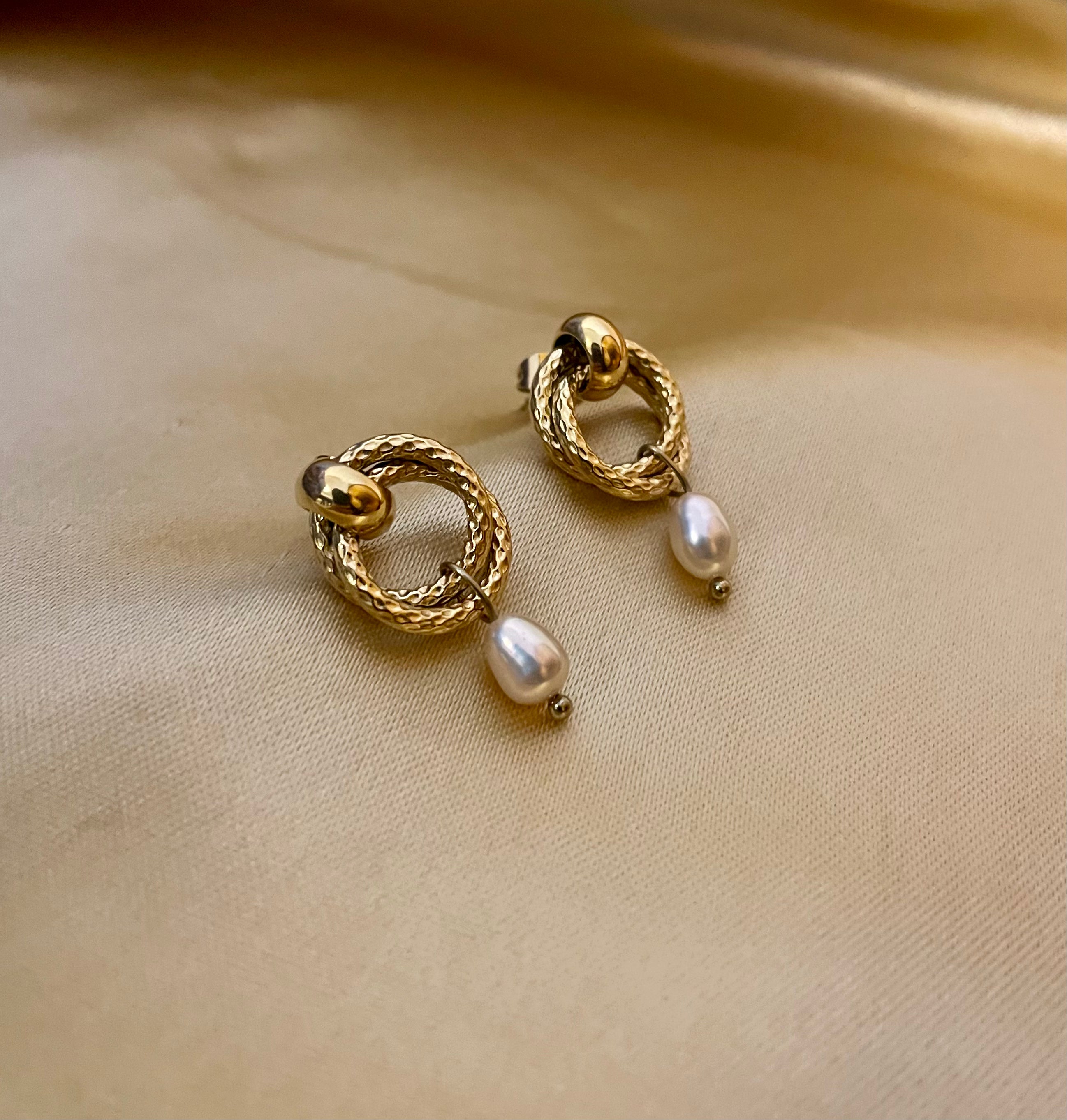 Women's textured gold interlocking hoop earrings with a genuine white pearl charm. High-resolution jewelry detail shot showing the clasp and finish.